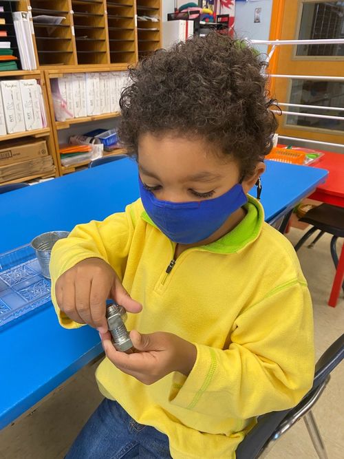 A student is focusing on holding a bolt and nut with curiosity to learn how it works.